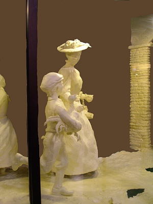 [A woman in a hat and a young boy holding a live duck all carved from butter.]